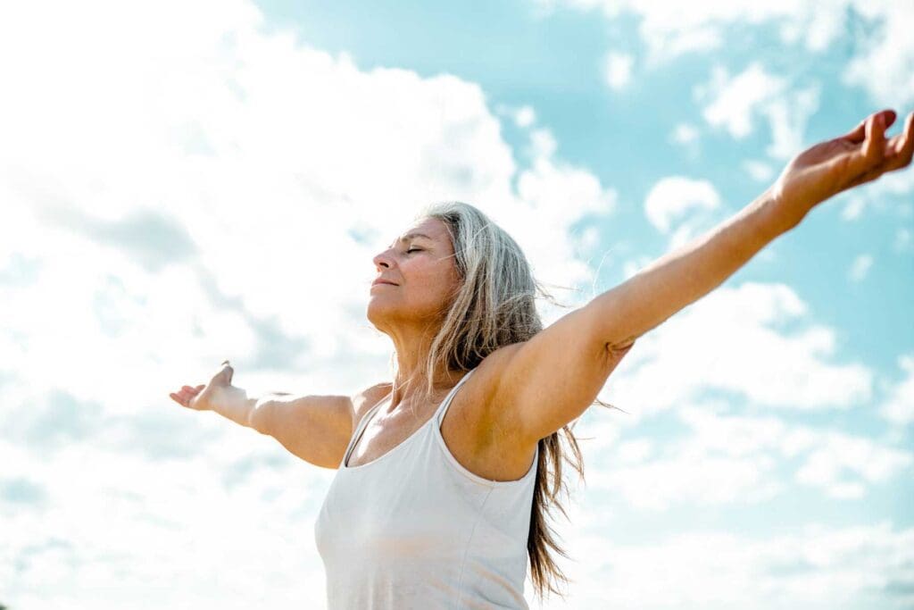 a senior woman outside on a sunny day standing with her arms stretched out