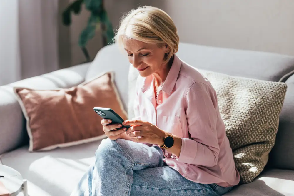 a senior woman sitting on the couch looking at her smart phone