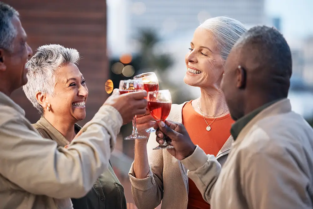A group of cheerful seniors at The Winsberg at Green Cay toast their wine glasses together during an outdoor social gathering, highlighting the engaging community lifestyle of maintenance-free senior living.